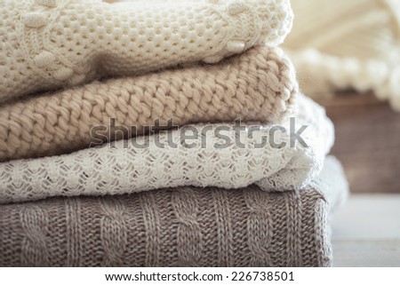 Stack of cozy knitted sweaters on a wooden table. Retro style. Warm concept