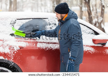 Transportation, winter, weather, people and vehicle concept - man cleaning snow from car with brush
