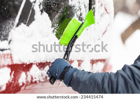Transportation, winter, weather, people and vehicle concept - man cleaning snow from car with brush