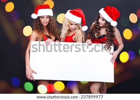 Three cheerful santa girls hold the blank placard with copy text. Christmas greetings card