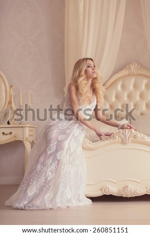 sexy glamour woman with blond hair in elegant dress posing in bedroom