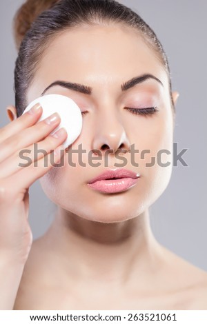 Portrait of woman using cotton pad over grey background