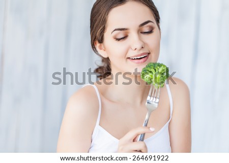 Portrait of happy smiling young beautiful woman eating broccoli