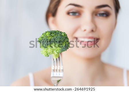 Portrait of happy smiling young beautiful woman eating broccoli