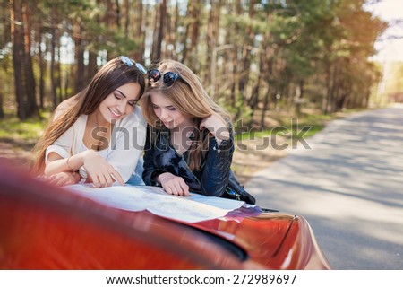 Happy friends on road trip reading a map on a summers day. Little holiday trip