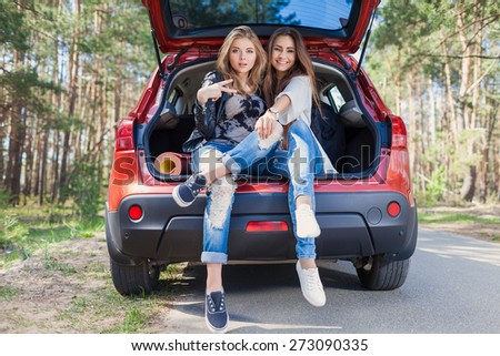 Young attractive woman sitting in the open trunk of a red car. Summer road trip