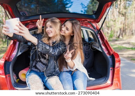 Young attractive woman sitting in the open trunk of a red car. Summer road trip