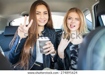 Happy friends with cup of coffee in car. Holiday trip of friends
