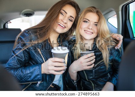 Happy friends with cup of coffee in car. Holiday trip of friends