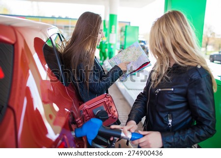 Happy friends holding map in gas station. Holiday trip of friends