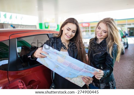 Happy friends holding map in gas station. Holiday trip of friends