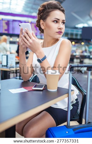 Young woman at international airport, drinking coffee while waiting for her flight. Female passenger at terminal, indoors.