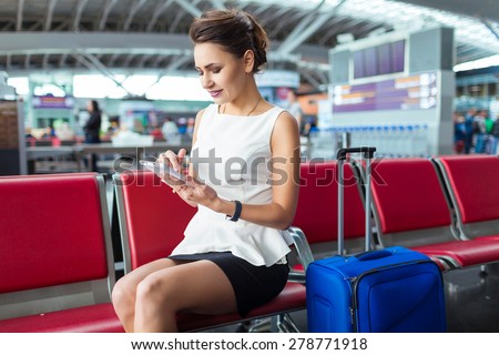 Young woman at international airport, sitting while waiting for flight. Female passenger at terminal, indoors.