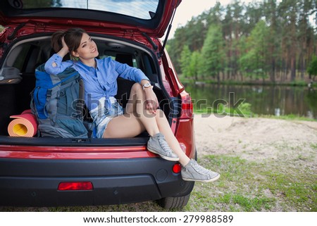 Happy young woman tourist travel on a red car to summer forest. Holiday trip to lake