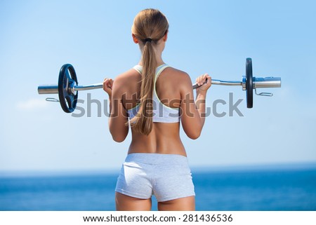 Rearview shot of a young woman doing squats with a barbell outside