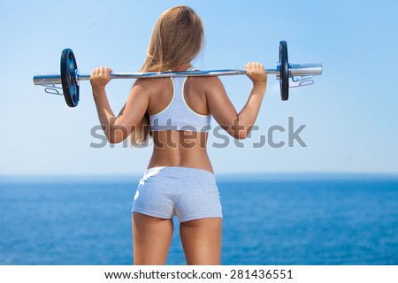 Rearview shot of a young woman doing squats with a barbell outside