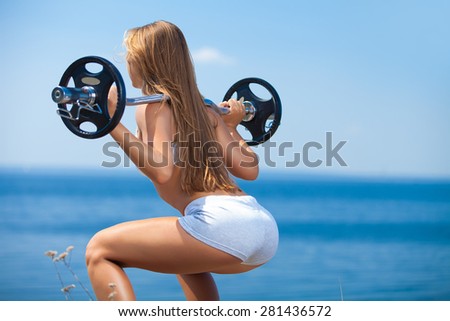 Rearview shot of a young woman doing squats with a barbell outside