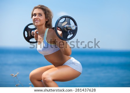 Shot of attractive young woman doing squats with a barbell outside