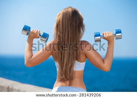 Shot of a beautiful young woman lifting weights outside