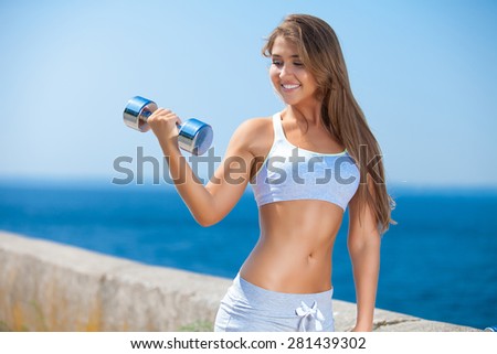 Shot of a beautiful young woman lifting weights outside