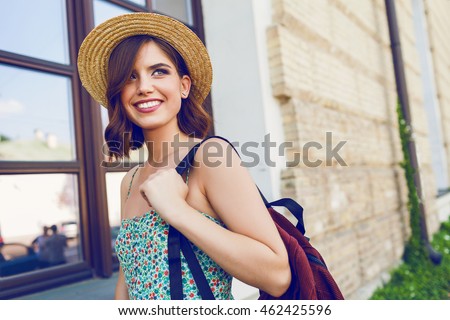 Sunny lifestyle fashion portrait of young stylish hipster woman walking on the street, wearing trendy outfit, straw hat, travel with backpack.