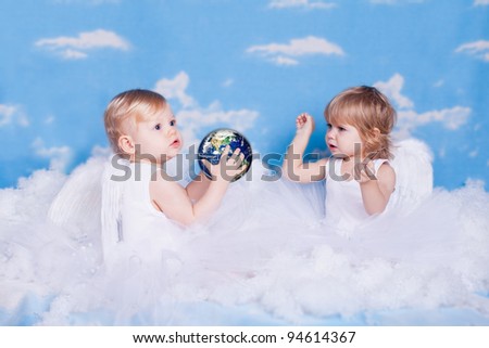 Two small children in the form of angels in the clouds playing with a toy \