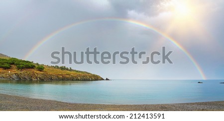 panorama of a rainbow, half over sea and land viewed from the pebble beach of Bernardi in the Mediterranean bay of Paulilles, Roussillon, Pyrenees Orientales, France