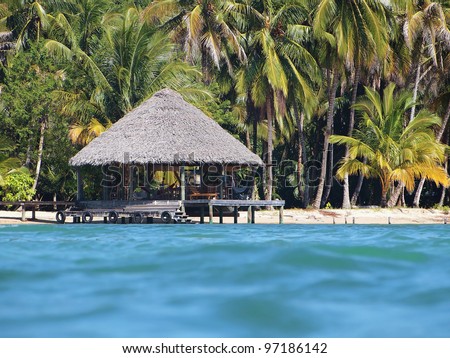Tropical beach hut overwater with thatch palm roof viewed from water surface, Caribbean sea