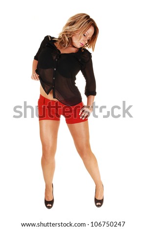 A very pretty and young woman standing in red shorts and black blouse and heels for white background in the studio.