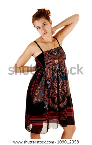 A pretty teenager in a black and color dress standing for white background with her hands behind her back.