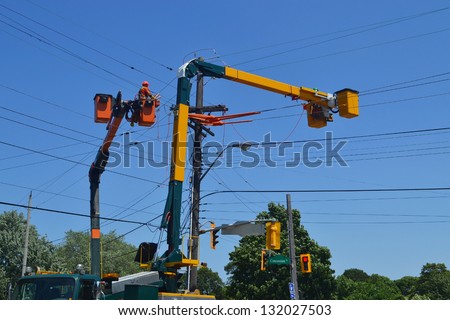 Hydro workers on a lift truck repairing hydro lines in Hamilton Ontario, under blue sky.