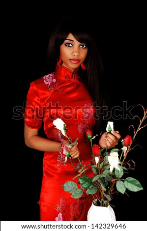 A lovely young black woman in a red Chinese dress for black background in profile holding some roses in her hand..