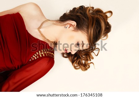A young pretty woman in a red dress lying whit her long curly hair for light beige background.