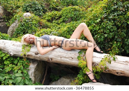 Pretty slim blond woman lying on a old loge in green plants in an black and  white bikini and take a sunbath on the rocky beach.