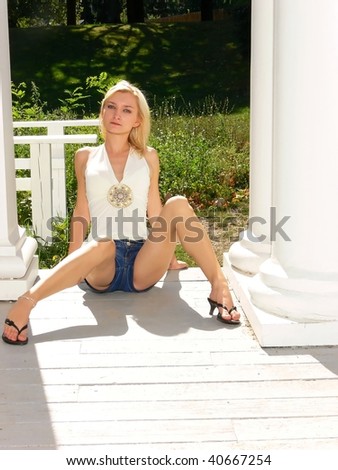 An young lady in short jeans and a white top sitting on the floor  beside two big white columns