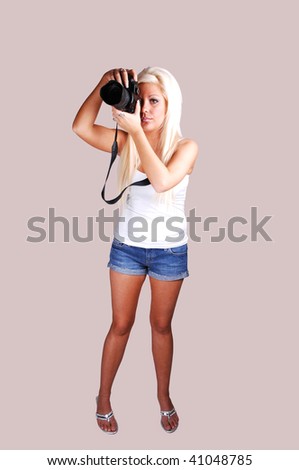 A pretty, young girl with long blond hair taking pictures in the studio in short shorts and white top, on light beige background.