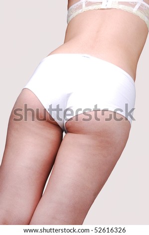 An young woman standing with her back to the camera in white boys cut panties for light gray background.