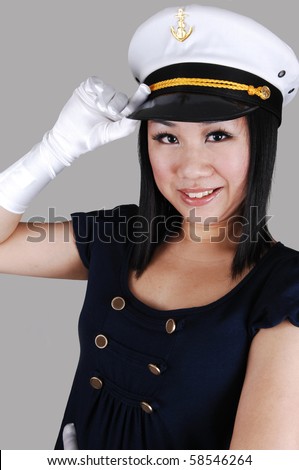A young pretty Asian woman with cloves with a sailors cap, navy blue shirt, saluting over light gray background.