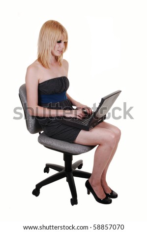 A pretty, blond young woman sitting on a office chair with a laptop on her lap and writing on the computer, on white background.