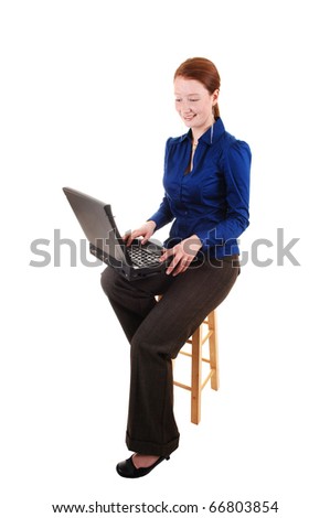 A business woman in a blue blouse and brown pants with a laptop on  her lap with her long red hair in the studio, for white background.