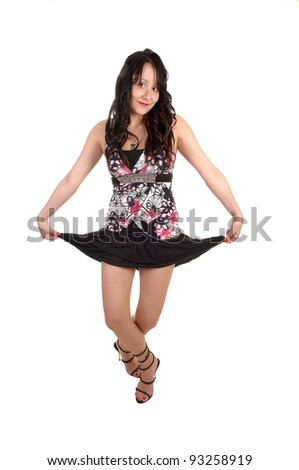 A young woman in a blouse and a short black skirt and with long curly black hair is dancing in the studio for white background.