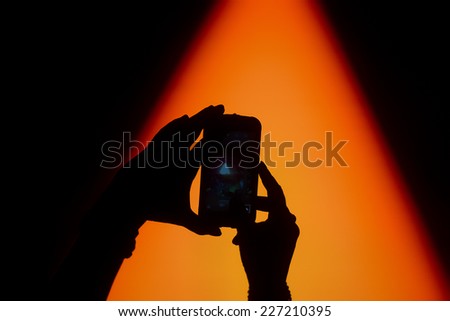 Silhouette of hands taking a photo with mobile phone on a concert with bright stage lights