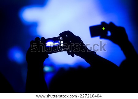 Silhouette of hands taking a photo with mobile phone on a concert with bright stage lights