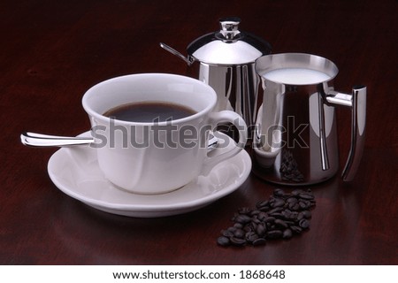A cup of coffee with a pitcher of cream, a sugar bowl, and a few coffee beans
