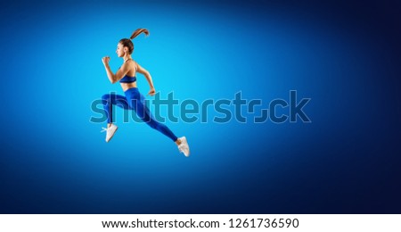 Young woman runner in blue sportwear jump in the air. Dynamic movement. Over blue background.