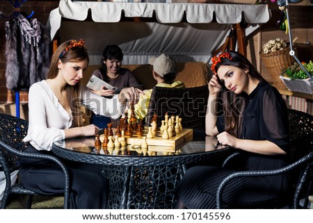 Two beautiful women play chess and think about strategy