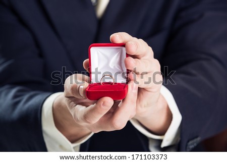 Close up of man holding wedding ring and gift box.