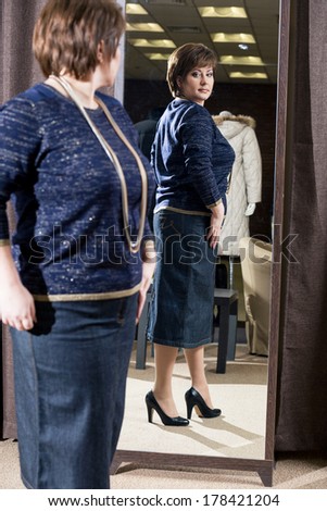 The woman of middle age tries on clothes at a mirror