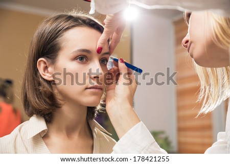 Make-up artist applying eyeshadow on model\'s eye and holding a shell with eyeshadow, close up