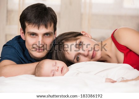 Smiling young couple and a little baby sleep in bed at home